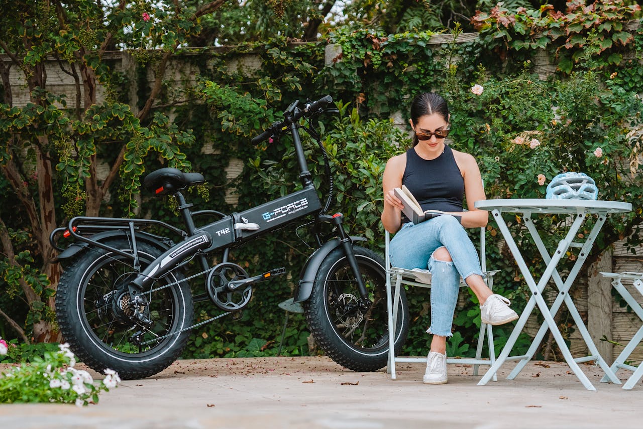 Home Woman in casual attire reading by an electric bike in a garden setting.